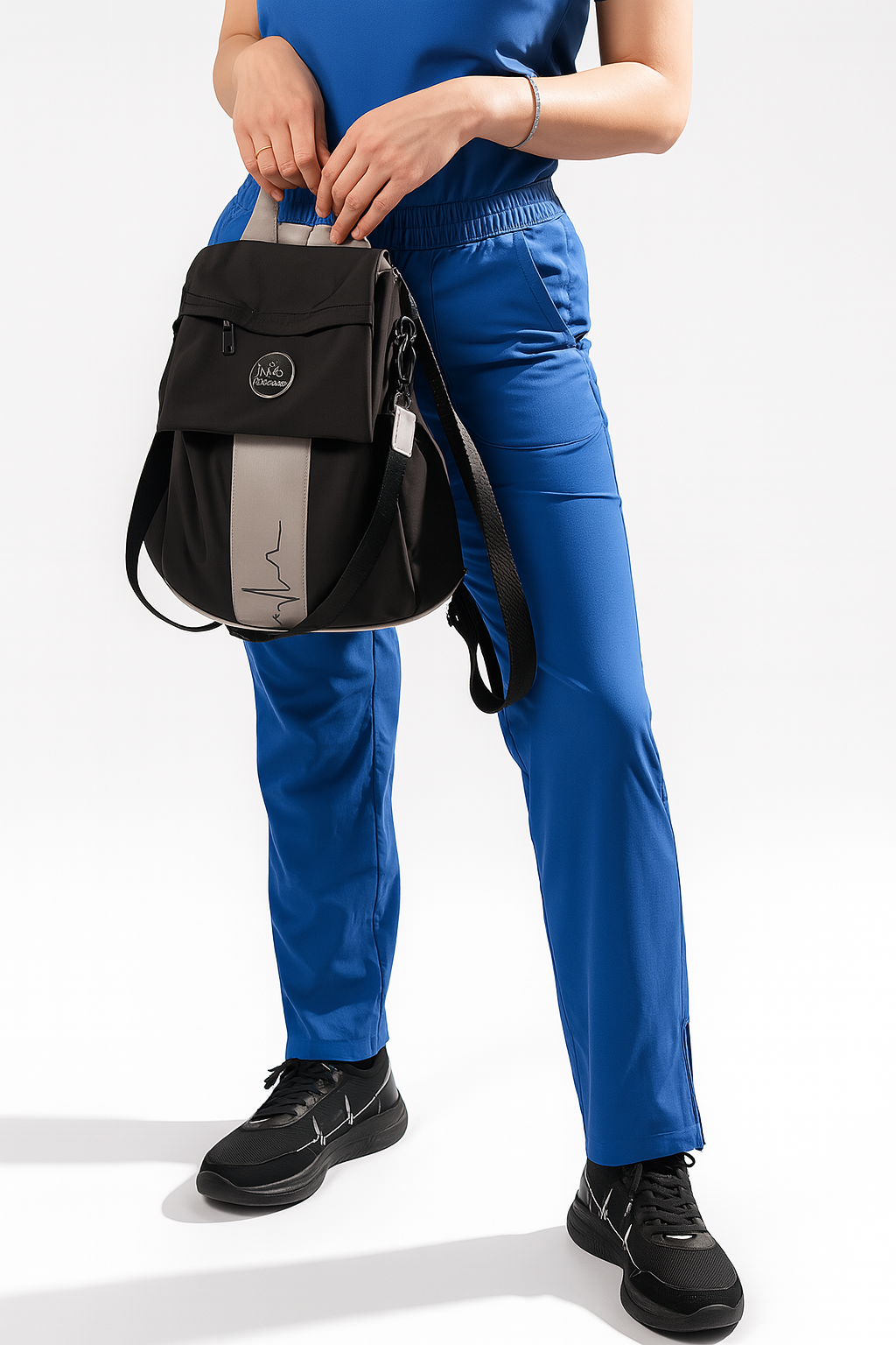 Person wearing MoxieGalia Premium Scrubs in blue, holding the MG Gidi-Up Lite backpack and wearing StandFX 12 sneakers on a white background.